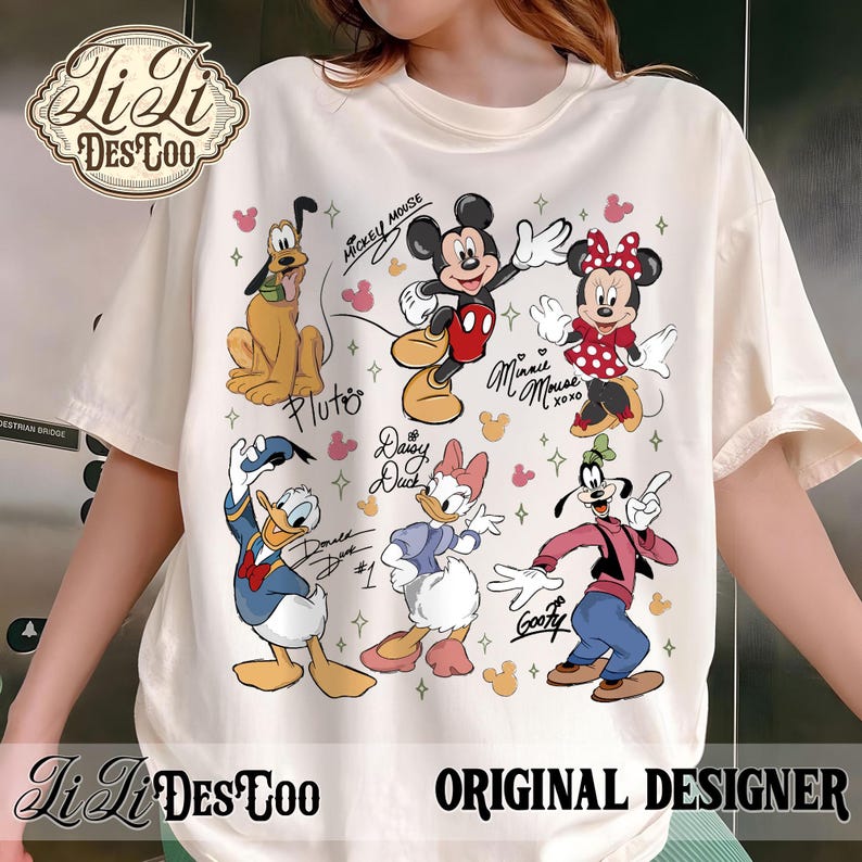 Puede incluir: Camiseta de color crema con los personajes de dibujos animados Mickey Mouse, Minnie Mouse, Pluto, Donald Duck, Daisy Duck y Goofy. La camiseta tiene el texto "Li Li DesToo ORIGINAL DESIGNER" y los nombres de los personajes. El dise&ntilde;o incluye corazones y estrellas rosas.