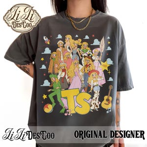 May include: A charcoal gray short-sleeve t-shirt featuring a large graphic print of multiple blonde characters in various outfits, including a green alien costume, a cowboy hat, and a pink dress, with the yellow letters TS and a guitar.