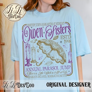 May include: A light blue t-shirt featuring a graphic print with the text "Rooftop Jump & Margaritas at Midnight", "Owen Sisters", "ESTD 1998", "Annual Parasol Jump", "There's a Little Witch in All of Us", and "Maria's Island, Massachusetts" with candles and a parasol.
