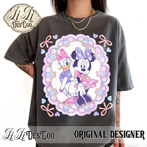 May include: Dark gray t-shirt featuring a colorful graphic of Minnie Mouse and Daisy Duck in a decorative frame with bows and hearts. The shirt has the text "Ji Li DesToo ORIGINAL DESIGNER" at the bottom.