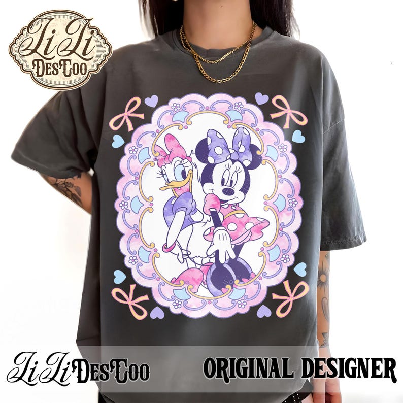 May include: Dark gray t-shirt featuring a colorful graphic of Minnie Mouse and Daisy Duck in a decorative frame with bows and hearts. The shirt has the text "Ji Li DesToo ORIGINAL DESIGNER" at the bottom.