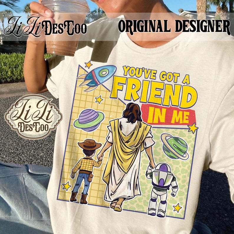 Puede incluir: Camiseta color crema con un gr&aacute;fico colorido con el texto "YOU'VE GOT A FRIEND IN ME". El dise&ntilde;o incluye un cohete, planetas y personajes de dibujos animados. La camiseta tiene cuello redondo.