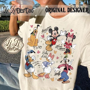 Puede incluir: Camiseta color crema con un gr&aacute;fico colorido de los personajes de Disney Mickey Mouse, Minnie Mouse, Pluto, Donald Duck, Daisy Duck y Goofy. La camiseta tiene el texto "ORIGINAL DESIGNER" y "Li Li Des Coo".