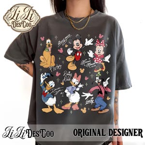 Puede incluir: Camiseta gris oscuro con un dise&ntilde;o colorido de personajes de Disney: Mickey y Minnie Mouse, Pluto, Donald y Daisy Duck y Goofy. La camiseta incluye el texto "Mickey Mouse", "Minnie Mouse xoxo", "Pluto", "Daisy Duck", "Donald Duck #1" y "Goofy".