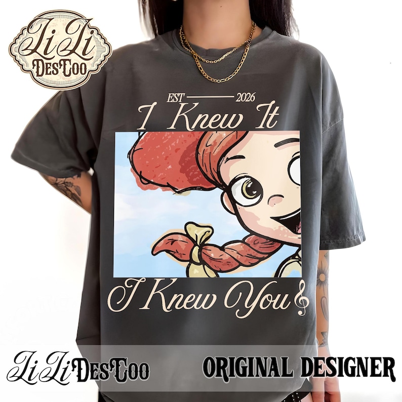 K&ouml;nnte beinhalten: Ein anthrazitfarbenes T-Shirt mit einem Grafikdruck einer Zeichentrickfigur mit roten Haaren und einem Zopf. Der Text lautet EST 2026, I Knew It und I Knew You. Das Design enth&auml;lt einen hellblauen Himmelshintergrund. Das Shirt hat einen Rundhalsausschnitt.