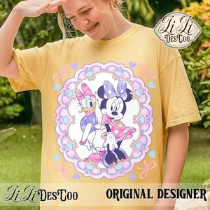 May include: Yellow t-shirt featuring a colorful graphic of Minnie Mouse and Daisy Duck inside a decorative frame with bows and hearts. The shirt has the text "Li Li DesCoo" and "ORIGINAL DESIGNER".