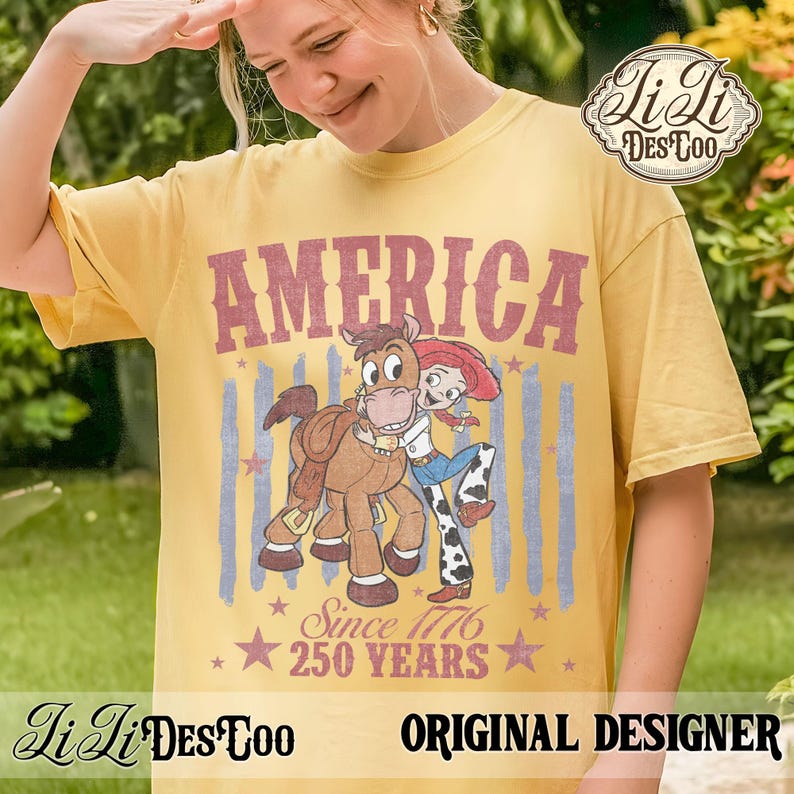 May include: A mustard yellow short-sleeve t-shirt featuring a graphic print with the text AMERICA, SINCE 1776, and 250 YEARS. The design includes a cartoon cowgirl hugging a brown horse, set against faded blue vertical stripes and red stars.
