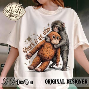 Puede incluir: Camiseta color crema con un diseño de dos monos abrazándose, con el texto "Punch is not alone." El diseño incluye estrellas y las palabras "Li Li DesToo" y "Original Designer."
