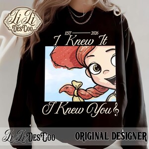 K&ouml;nnte beinhalten: Ein schwarzes Langarm-Sweatshirt mit einem Grafikdruck einer Zeichentrickfigur mit roten Haaren in einem Zopf. Der Text lautet EST 2026, I Knew It und I Knew You. Das Design enth&auml;lt ein Logo in der oberen linken Ecke mit LiLi DES TOO.