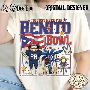 May include: Cream-colored t-shirt with a graphic design featuring the text "I'M JUST HERE FOR BENITO BOWL". The design includes a frog in a football uniform holding a Puerto Rican flag, and other cartoon elements. The shirt also has the text "PR".