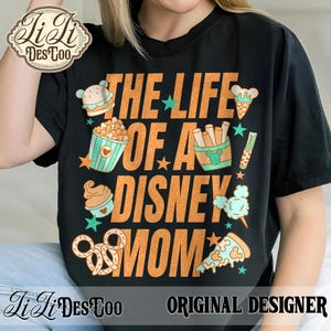 May include: Black t-shirt with the text "THE LIFE OF A DISNEY MOM" in orange. The shirt features illustrations of Disney-themed snacks like popcorn, ice cream, and pizza. The shirt also has the text "ORIGINAL DESIGNER".
