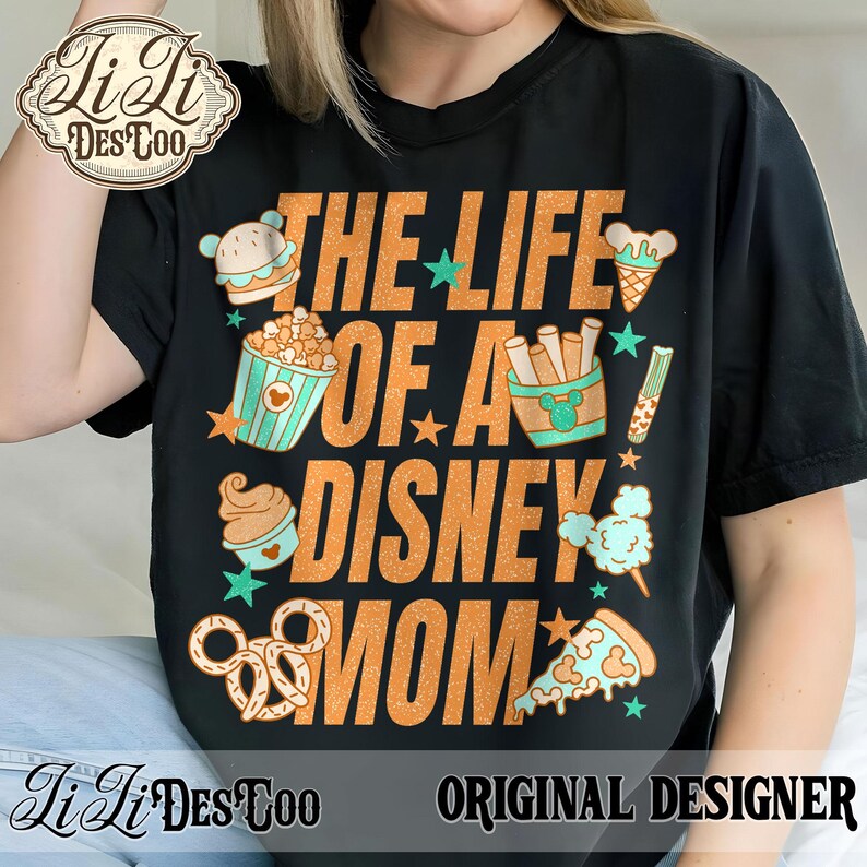 May include: Black t-shirt with the text "THE LIFE OF A DISNEY MOM" in orange. The shirt features illustrations of Disney-themed snacks like popcorn, ice cream, and pizza. The shirt also has the text "ORIGINAL DESIGNER".