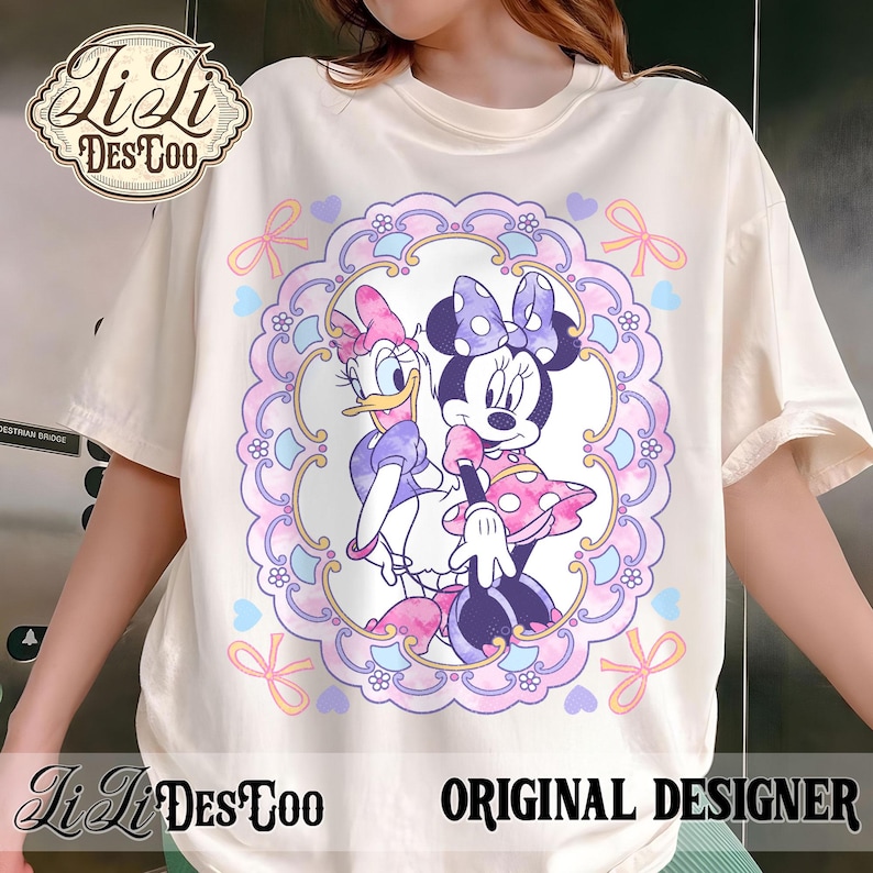May include: Cream-colored t-shirt featuring a circular design with Minnie Mouse and Daisy Duck. The design is framed by a pink and purple border with bows and hearts. The shirt also has the text "LiLi DesToo ORIGINAL DESIGNER".