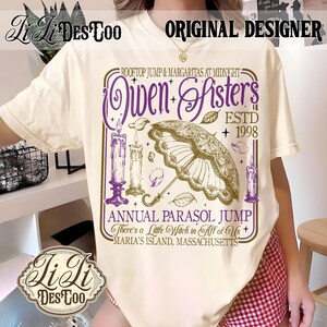 May include: A cream-colored t-shirt featuring a graphic print with purple and gold text that reads Owen Sisters, Rooftop Jump & Margaritas at Midnight, Estd 1998, Annual Parasol Jump, There's a Little Witch in All of Us, Maria's Island, Massachusetts.