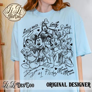 May include: Light blue t-shirt featuring a black and white sketch of Mickey Mouse, Minnie Mouse, Donald Duck, Daisy Duck, Goofy, and Pluto. The shirt includes the characters' signatures and the text "Original Designer."