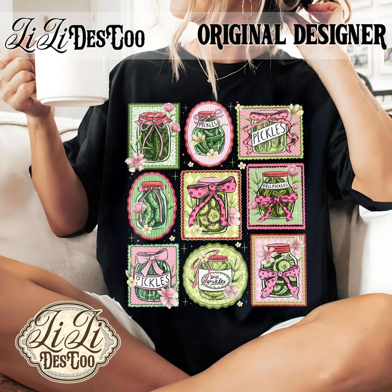 May include: Black t-shirt featuring a colorful graphic of pickle jars with pink bows and floral accents. The text "PICKLES" and "Dill Pickles" are visible on some jars. The shirt also has the text "Li Li Des Too" and "ORIGINAL DESIGNER".