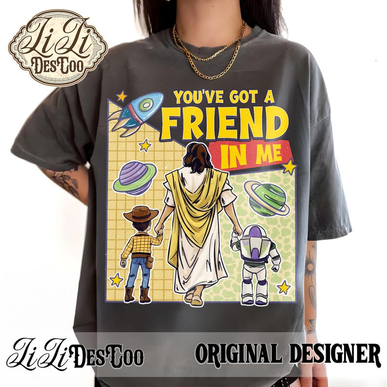 Puede incluir: Camiseta gris oscuro con un gr&aacute;fico colorido que presenta el texto "YOU'VE GOT A FRIEND IN ME". El dise&ntilde;o incluye un cohete, planetas, estrellas y personajes de dibujos animados. La camiseta tambi&eacute;n tiene el texto "Li Li Des Too Original Designer".