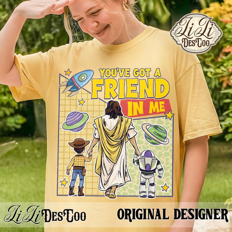 Puede incluir: Camiseta amarilla mostaza con el texto "YOU'VE GOT A FRIEND IN ME" y un gr&aacute;fico de Jes&uacute;s tomados de la mano con dos personajes de dibujos animados. El dise&ntilde;o incluye un cohete, planetas y estrellas. La camiseta tiene el logo "LiLi DesCoo" y el texto "ORIGINAL DESIGNER".