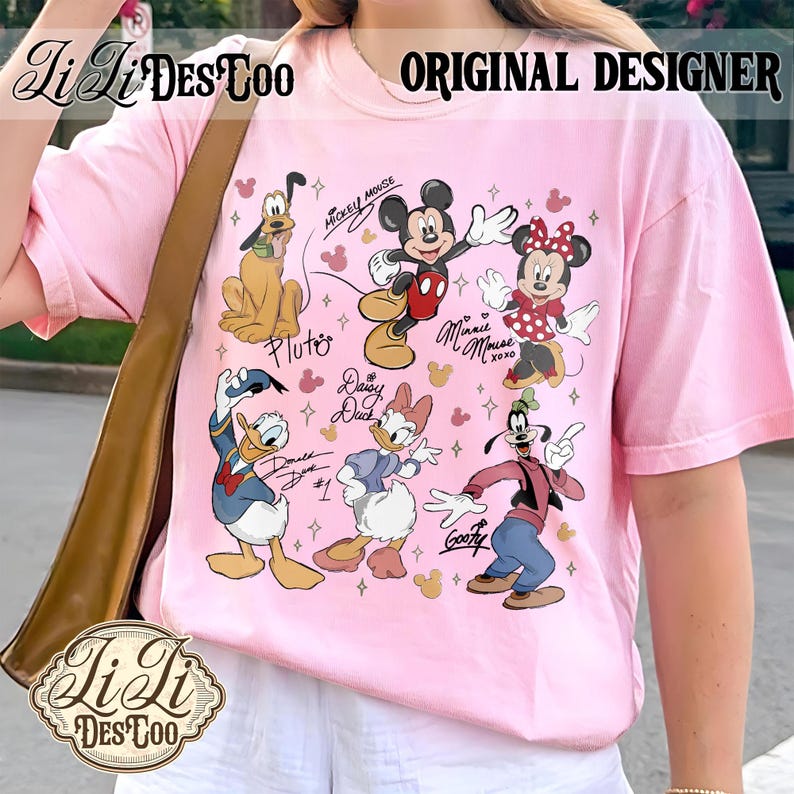 Puede incluir: Una camiseta rosa claro con un gr&aacute;fico colorido de personajes de Disney, incluyendo Mickey Mouse, Minnie Mouse, Pluto, Donald Duck, Daisy Duck y Goofy. La camiseta tiene el texto "ORIGINAL DESIGNER" en la parte superior.