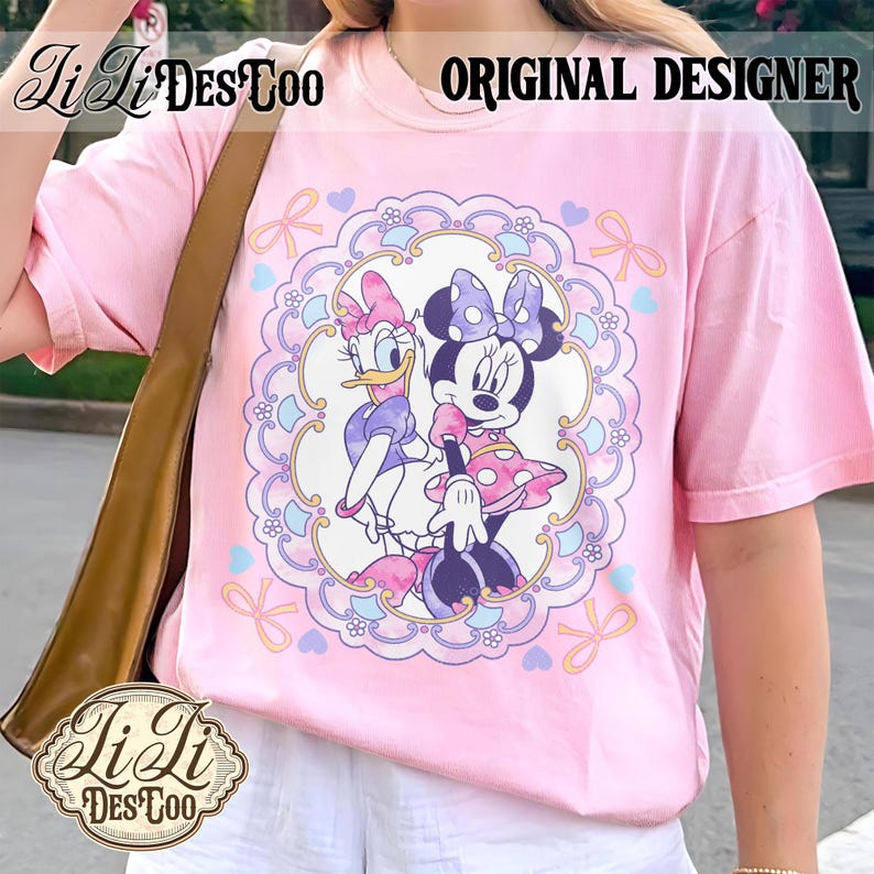 May include: Pink t-shirt featuring a Minnie Mouse and Daisy Duck graphic. The design is framed by a decorative border with hearts and bows. The shirt also has the text "ORIGINAL DESIGNER" and the brand logo "LiLi DesToo".