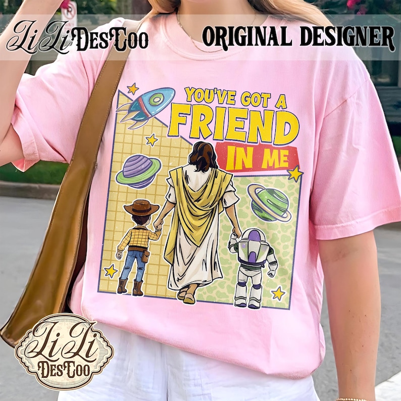 Puede incluir: Camiseta rosa claro con un dise&ntilde;o gr&aacute;fico que incluye el texto "YOU'VE GOT A FRIEND IN ME", un cohete, planetas y personajes de dibujos animados. La camiseta tambi&eacute;n tiene el texto "ORIGINAL DESIGNER" y la marca "Li Li DesCoo".