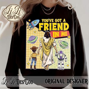 Puede incluir: Sudadera negra con un gr&aacute;fico colorido con el texto "YOU'VE GOT A FRIEND IN ME". El dise&ntilde;o incluye un cohete, planetas y personajes de dibujos animados. La sudadera tiene el texto "Li Li Des Too" y "ORIGINAL DESIGNER".