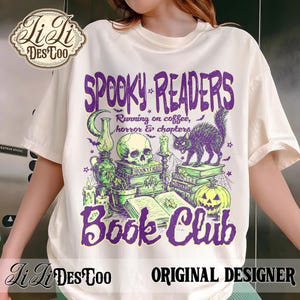 May include: A cream-colored short-sleeve t-shirt featuring a graphic print with the text "SPOOKY READERS BOOK CLUB" and "Running on coffee, horror & chapters." The design includes a skull, a black cat, a jack-o'-lantern, books, and candles.