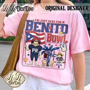 May include: Pink t-shirt with the text "I'M JUST HERE FOR BENITO BOWL". The graphic includes a frog in a football uniform holding a Puerto Rican flag, a bunny, and other cartoon elements. The words "ORIGINAL DESIGNER" are at the top.