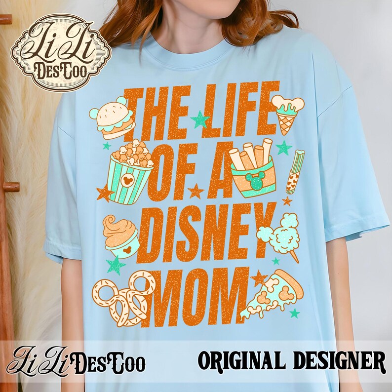 May include: Light blue t-shirt with the text "THE LIFE OF A DISNEY MOM" in orange. The shirt features cartoon illustrations of Disney-themed snacks like popcorn, ice cream, and pizza. The words "ORIGINAL DESIGNER" are also printed on the shirt.