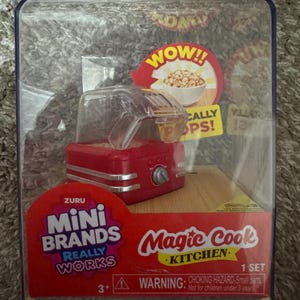 以下が含まれることがあります： 透明なプラスチックパッケージに入った、赤いMini Brands Magic Cook Kitchenのおもちゃセット。おもちゃは、赤い外観にシルバーのアクセントと透明な蓋が付いています。パッケージには「WOW!!」と「REALLY WORKS」の文字が含まれています。
