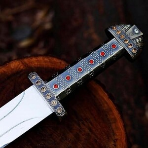May include: A silver and black sword with a red and gold handle. The handle is decorated with a geometric pattern and red gemstones.