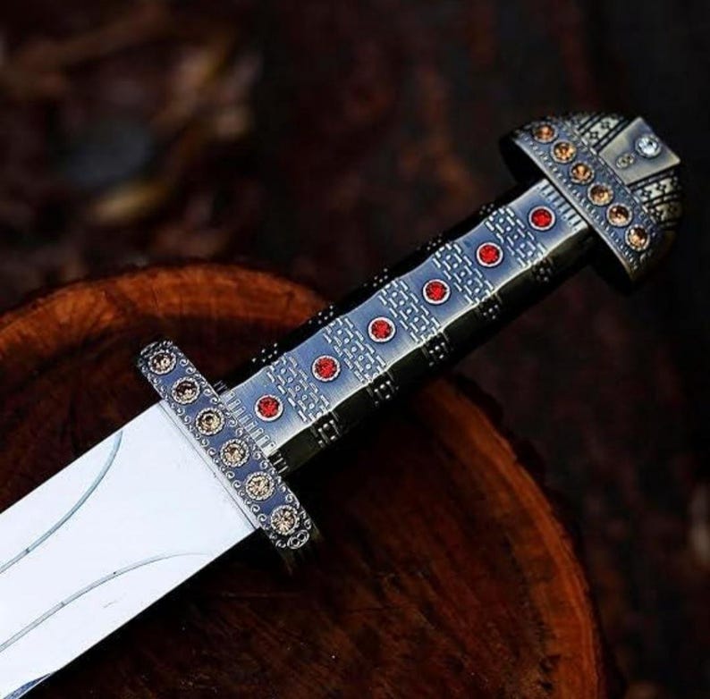 May include: A silver and black sword with a red and gold handle. The handle is decorated with a geometric pattern and red gemstones.