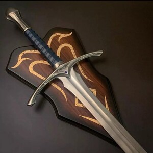 May include: A silver sword with a blue and silver handle, mounted on a wooden plaque with gold accents. The plaque has a decorative design with swirling lines.