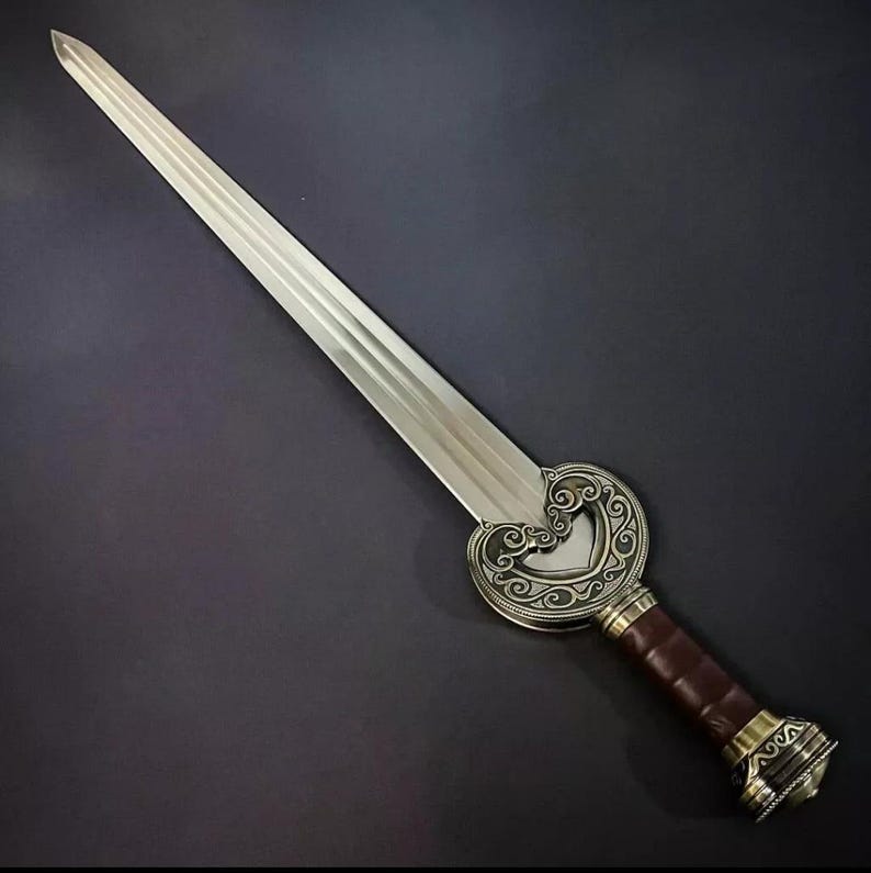 May include: A silver sword with a decorative, ornate, heart-shaped guard and a brown leather handle. The handle has a gold-colored metal pommel with intricate designs.