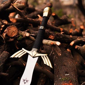 May include: A gold and silver sword with a black handle, lying on a pile of brown branches.