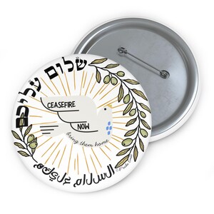 May include: A white button featuring a dove carrying the words "CEASEFIRE NOW bring them home" in black text. The dove is surrounded by olive branches and the words "שלום עליכם" and "السَّلاَمُ عَلَيْكُمْ" in Hebrew and Arabic.
