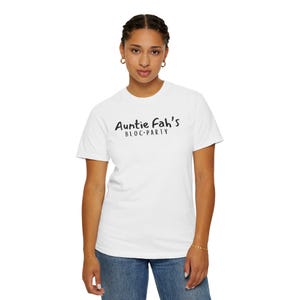 May include: White t-shirt with the text "Auntie Fah's BLOC-PARTY" in black script. The shirt is being worn by a person in blue jeans. The person is wearing gold hoop earrings and a gold bracelet.