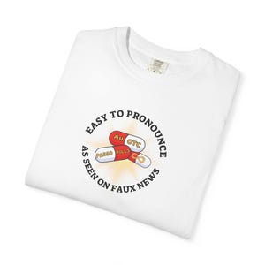 May include: White t-shirt with a circular graphic featuring three pill capsules in red, white, and gold. The text around the pills reads "EASY TO PRONOUNCE" and "AS SEEN ON FAUX NEWS."