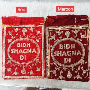 May include: Two rectangular velvet drawstring pouches, one red and one maroon, each featuring gold embroidered floral patterns and the text BIDH SHAGNA DI centered within a circular gold sequin border. Both bags have gold drawstring closures.