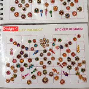 May include: A collection of adhesive sticker kumkum bindi ornaments arranged on two white grid-patterned sheets. The decorative pieces feature various circular, floral, and elongated shapes in vibrant colours including red, blue, green, pink, and gold.