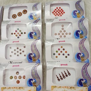 May include: Eight individual retail packages of adhesive bindi stickers, each featuring a variety of circular, floral, and teardrop-shaped designs in assorted colors like red, gold, green, and blue, displayed on white cards with peacock graphics.