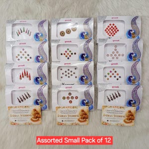 May include: Twelve individual white cardboard display cards, each featuring a unique arrangement of small adhesive bindi stickers in various colors and shapes, with the text INDIAN WEDDING printed on the bottom of each card.
