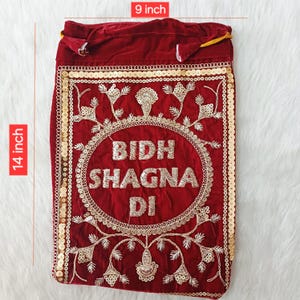 May include: A deep red velvet drawstring pouch featuring gold sequin borders and intricate gold embroidery. The centre displays the text BIDH SHAGNA DI in gold lettering. The pouch measures 9 inches in width and 14 inches in height.