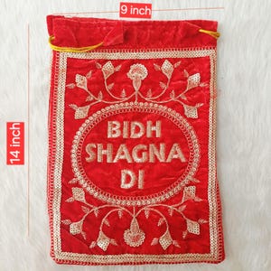 May include: A red velvet drawstring pouch measuring 9 inches wide by 14 inches high. The front features gold embroidered floral patterns and the text BIDH SHAGNA DI enclosed in a circular border with gold sequin trim along the edges.