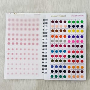 May include: A spiral-bound booklet containing sheets of adhesive circular stickers in various solid colors. The right page displays rows of multicolored dots with the text A QUALITY PRODUCT and STICKER KUMKUM printed at the top.