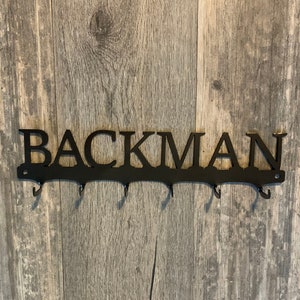 May include: Black metal key rack with the name "BACKMAN" in large letters and five hooks.