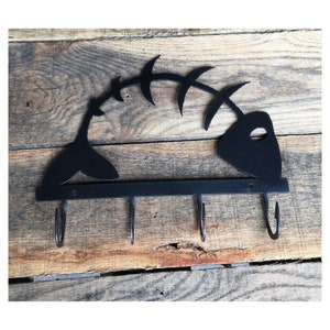May include: Black metal fish skeleton key holder with four hooks. The fish skeleton is mounted on a wooden surface.