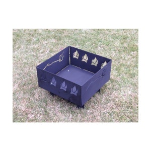 May include: Black metal fire pit with a square shape and decorative cutouts of flames. The fire pit has four legs and is sitting on a grassy surface.