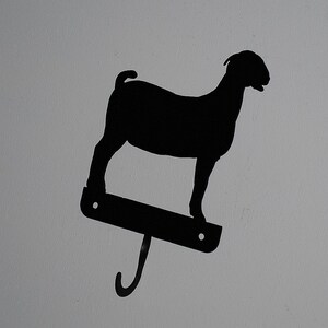 May include: Black metal goat silhouette wall hook. The goat is standing on a metal base with a hook extending from the bottom.