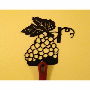 May include: Black metal grapevine wall hook with a red handle. The hook is shaped like a bunch of grapes with a leaf.